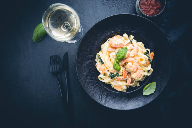 Italian pasta fettuccine in a creamy sauce with shrimp on a black plate, top view