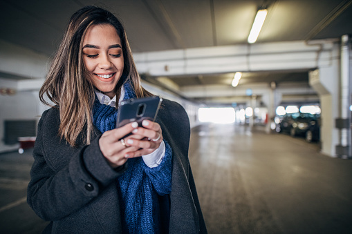 One beautiful young woman standing in underground parking garage and using smart phone