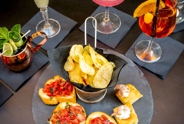 A typical Italian aperitif with bruschetta and drink Rome, Italy -- A typical Italian aperitif with bruschetta, potato chips, vegetable snack and a colored drink, served on a slate plate. aperitif photos stock pictures, royalty-free photos & images