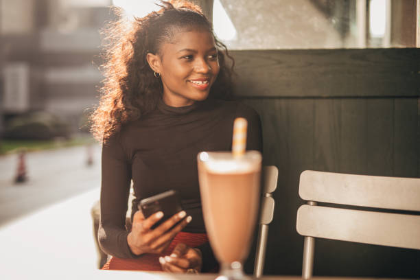 istock Black woman sitting alone in sidewalk cafe and using smart phone 1204155938