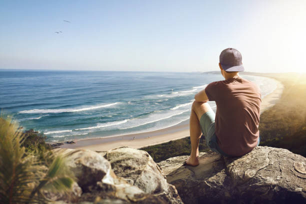 istock Young man sitting on a rock above a beautiful coastline 1204159149