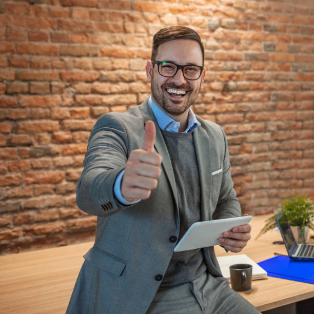 istock Cheerful businessman thumbs up posing and smiling at camera. 1204159974