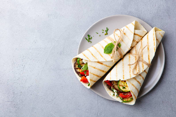 Wrap sandwich with grilled vegetables and feta cheese on a plate. Grey background. Copy space. Top view. stock photo
