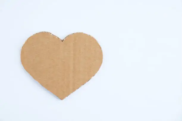 Photo of Heart symbol made of brown cardboard with jagged edges on white background.