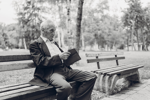 Elderly gentleman sitting in a park and reading his note pad.