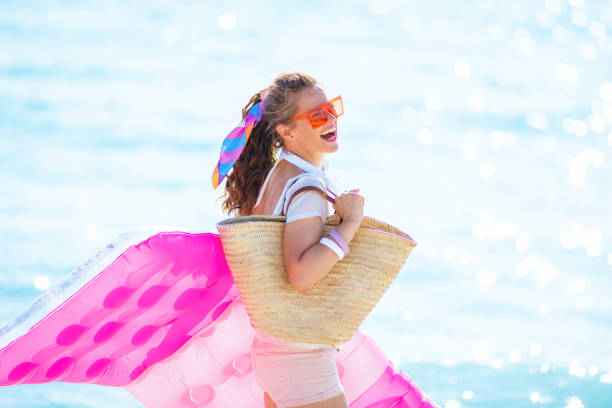 mujer alegre en la costa del océano sosteniendo colchón inflable - tropical climate audio fotografías e imágenes de stock