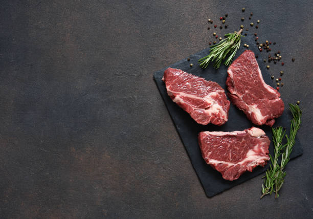 Raw marbled beef steak on a stone board. Spices, dishes. Top view flat lay with copy space.
