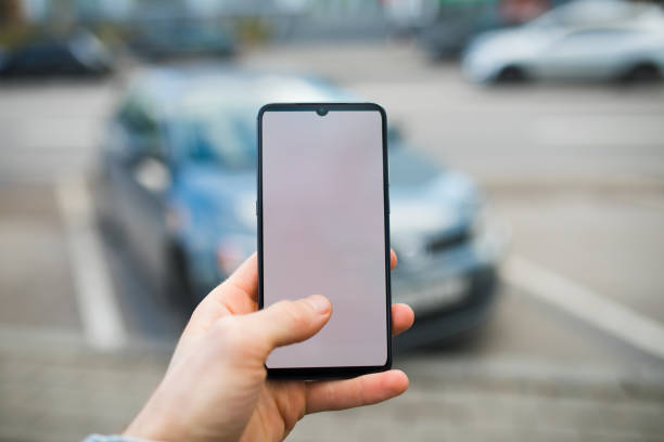 istock Hand holding smartphone with blank display in city, car on background 1204165884