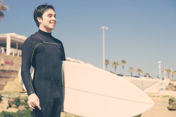 istock Smiling handsome man holding surfboard on sunny beach 1204166045