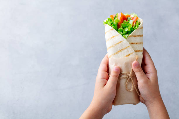 avvolgere il panino nelle mani dei bambini. sfondo in pietra grigia. vista dall'alto. copiare lo spazio. - sandwich healthy eating wrap sandwich food foto e immagini stock