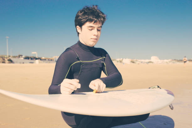 istock Serious young man cleaning surfboard on sunny beach 1204166883