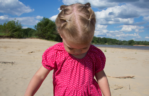 Bowed head of caucasian child of two years old walking on sand beach in summertime