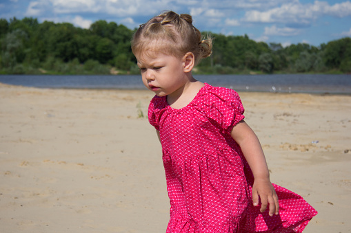 Portrait of unhappy caucasian child of two years old walking on sand beach in summertime