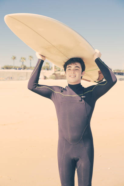 istock Smiling man holding surfboard on head on sunny beach 1204166923
