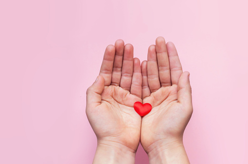 Hands of child holding small Red Heart on pink background with copy space