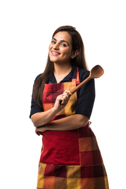 Indian / asian woman chef wearing Apron and holding wooden spatula while standing isolated over white background stock photo