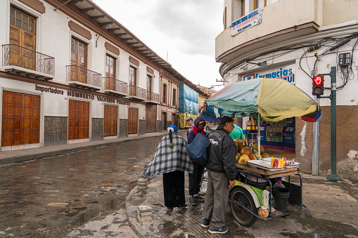 Cuenca, Ecuador - March 3, 2019: Locals getting coconut drink at mobile street kiosk during raining time in Cuenca.  Cuenca is the most beautiful colonial town in Ecuador. The center of the city is listed as an UNESCO World Heritage Site due to its many historical buildings and is on approximately on  2,560 meters above sea level.