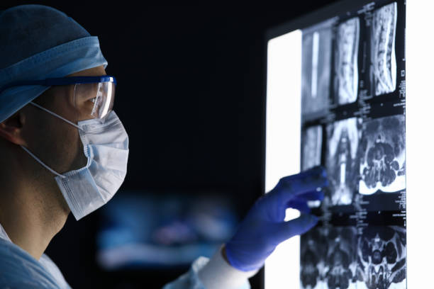 männlicher arzt in chirurgischer kleidung mit blick auf wirbel mri scan - krebs tumor stock-fotos und bilder
