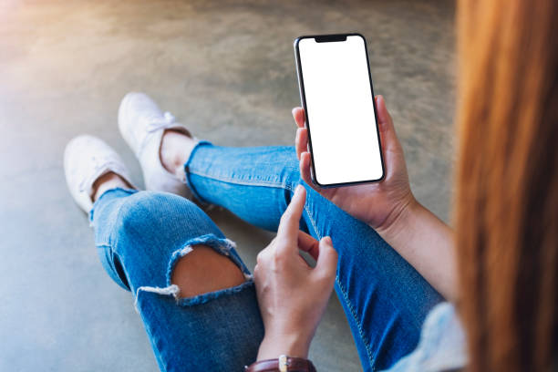 istock a woman holding black mobile phone with blank white screen while sitting on the floor 1204177997