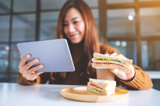 istock woman holding and eating whole wheat sandwich while using tablet pc 1204178008