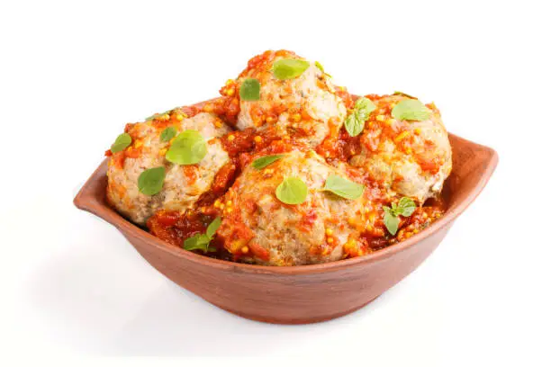 Photo of Pork meatballs with tomato sauce, oregano leaves, spices and herbs in clay bowl isolated on white background. side view, close up.