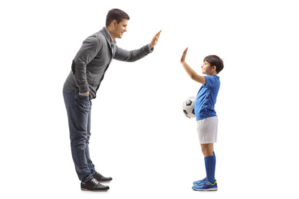 istock Boy with a soccer ball gesturing high five with a man 1204185152