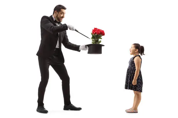 Full length shot of a magician making flowers appear from a hat and a surprised little girl watching isolated on white background