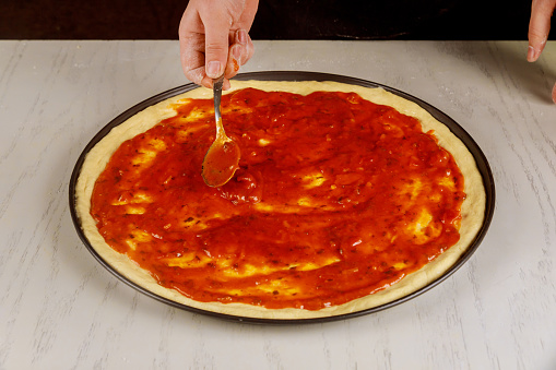 Chef coversraw pizza dough with marinara sauce.