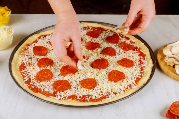 istock Woman putting mushrooms on raw uncooked pizza. 1204186021