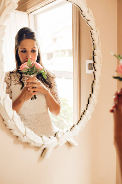 istock Bride before the wedding looking at smelling her roses wedding bouquet in the mirror nervously. Important day. Wedding and marry concept. 1204187496