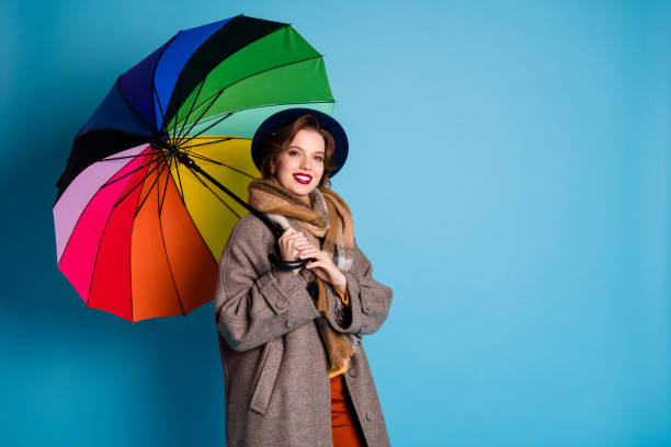 la pluie ne m’arrêtera pas. photo de la jolie dame de voyageur retiennent le parasol coloré marchant en bas de l’usure de rue l’élégant long gris gris de manteau gris de pantalon de chapeau écharpe de couleur bleue d’isolement - rain women umbrella parasol photos et images de collection