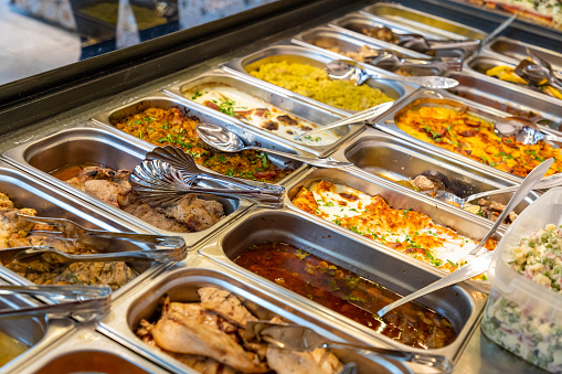 Variety of cooked food in steel trays with serving utensils in buffet