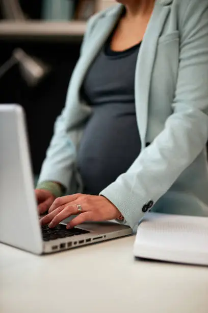 Close up of dedicated caucasian pregnant businesswoman standing in her office and checking an email from important client. Hands are on keyboard.