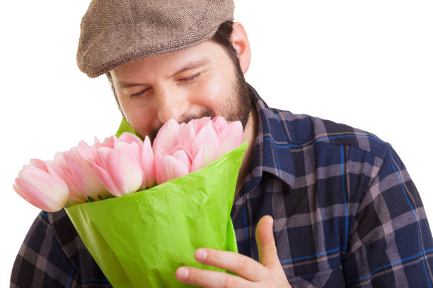 ひげを生やした若いハンサムな男がピンクのチューリップの花束を持ち、白い背景に孤立した目を閉じた匂いを嗅いだ。母の日、バレンタインデー、イースターと驚きのコンセプト。 - single flower flower mothers day easter ストックフォトと画像