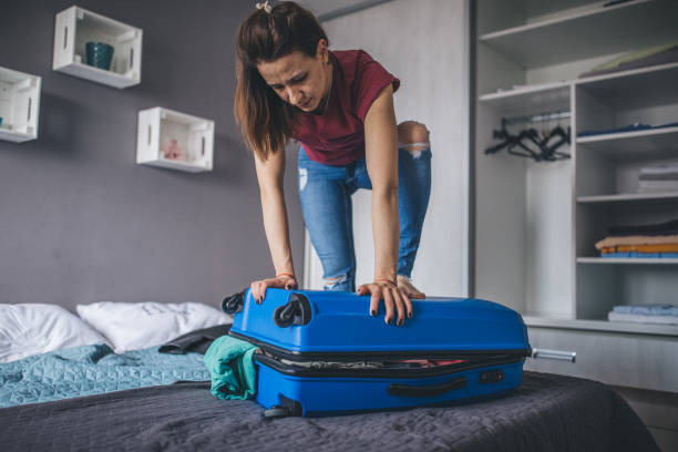 istock One woman trying to close overpacked suitcase 1204191084