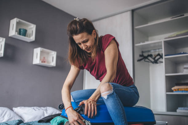istock Woman trying to close suitcase 1204191196