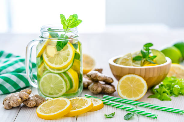 Lemon and ginger infused water on white table Front view of a mason jar filled with lemon and ginger infused water shot on white table. Some lemon slices, ginger roots and two green and white drinking straws complete the composition. Predominant colors are yellow, green and white. High resolution 42Mp studio digital capture taken with Sony A7rii and Sony FE 90mm f2.8 macro G OSS lens lime photos stock pictures, royalty-free photos & images