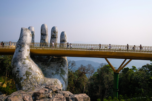 Danang, Vietnam - April 20, 2019 - Tourists walk on the Golden Bridge in Ba Na Hills, supported by a pair of giant hands. The bridge located 1,400 meters above sea level with hill scenery