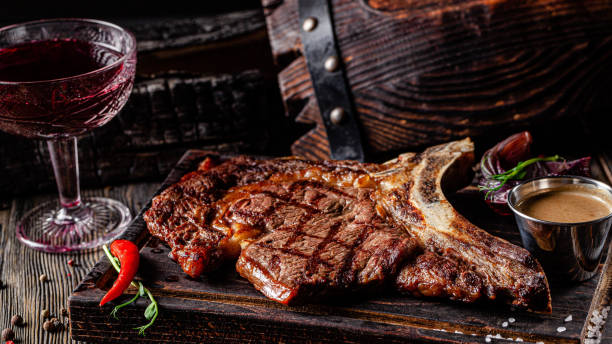 european cuisine in ukrainian style. large, juicy grilled t-bone steak. serving dishes in a restaurant on a wooden board with sauce. background image, copy space text - veal t bone steak raw steak imagens e fotografias de stock