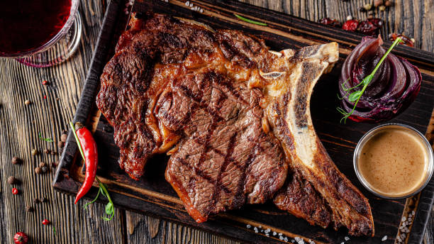 european cuisine in ukrainian style. large, juicy grilled t-bone steak. serving dishes in a restaurant on a wooden board with sauce. background image, copy space text - veal t bone steak raw steak imagens e fotografias de stock