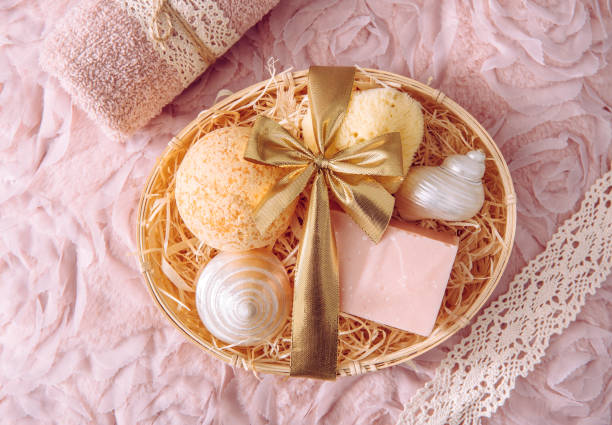 Natural bamboo material gift basket filled with shredded wood excelsior with various spa bathroom products, pink soap bar, bath bomb, natural sponge on vintage light pink background. Beauty present.