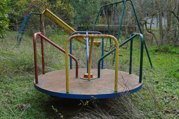 Playground in overgrown garden of an abandoned house. Rusty merry-go-round swings and slide.