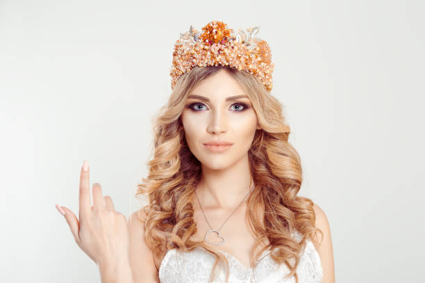 istock Woman with the crown shows come here gestures with her index finger right hand, white background. Woman wearing crown, bride princess miss picture for beauty magazines white light gray background wall 1204227511