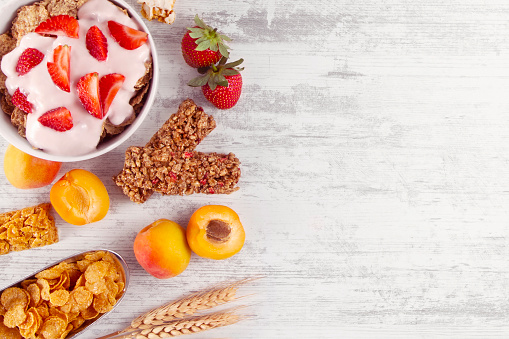 Breakfast cereal with granola bar and strawberries on white wooden table