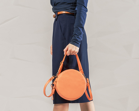 Stylish fashionable woman with trendy leather round orange handbag bag. Model wearing classic blue long sleeve and pencil skirt. Clothing and accessories