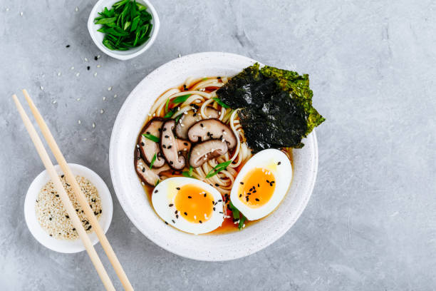 Asian Vegetarian Udon or Ramen noodles soup in bowl with Shiitake mushrooms, boiled eggs and nori sheets Asian Vegetarian Udon or Ramen noodles soup in bowl with Shiitake mushrooms, boiled eggs and nori sheets on grey stone background. Top view, copy space. shiitake mushroom photos stock pictures, royalty-free photos & images