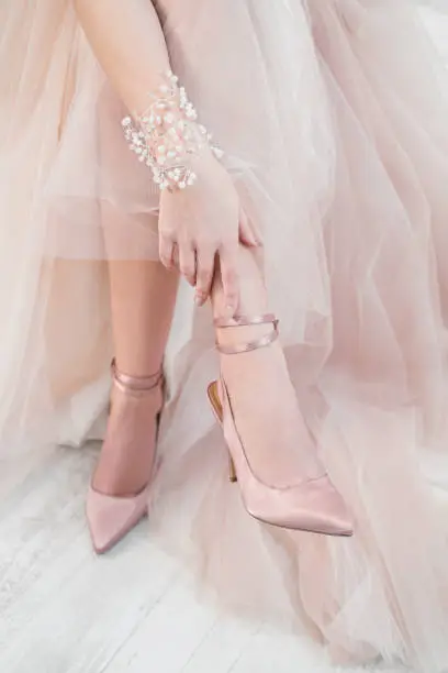 Photo of The woman bride puts shoes on her leg. Wedding dress and shoes.