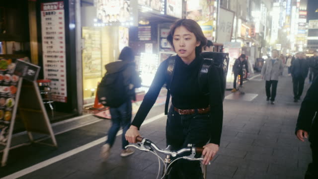 Japanese female food courier looking for the delivery address in Tokyo (slow motion)