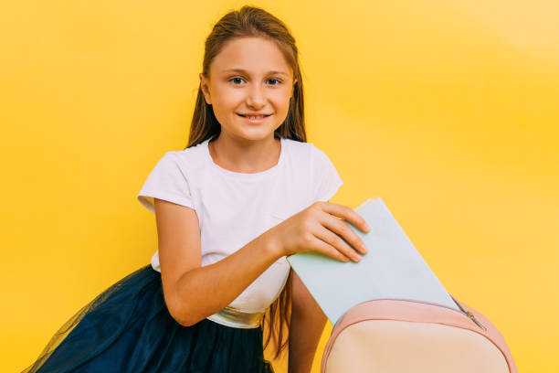 fille d’école dans des vêtements d’école sur un fond jaune - schoolgirl child backpack book bag photos et images de collection