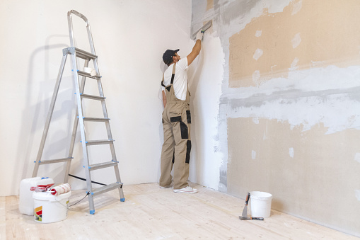 Male painter with a spatula in his hands makes repairs in  home. Room renovation concept.